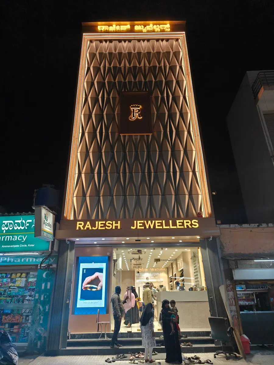 The shop at night: a tall bronze diamond-lattice front with a lit R monogram above the sign.