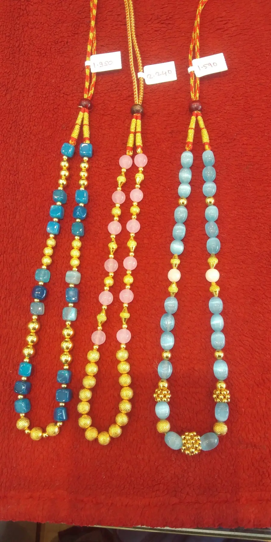 Gold chains strung with turquoise, rose and white beads, laid on red cloth.