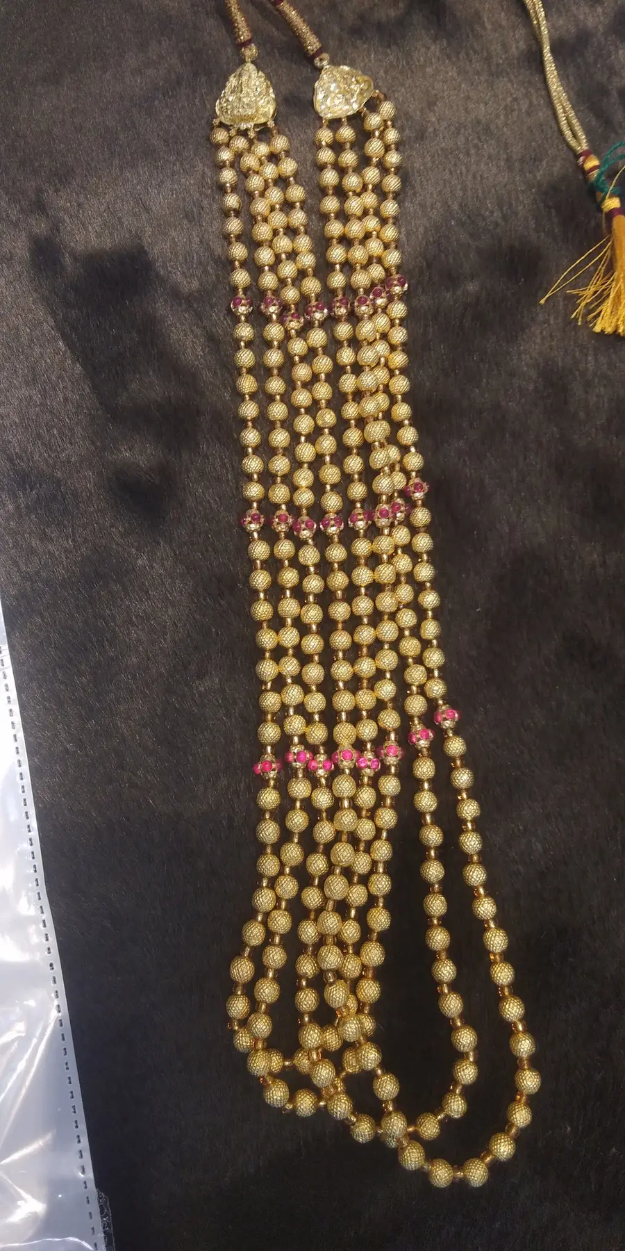 Several strands of small gold beads with pink stone stations, laid side by side.